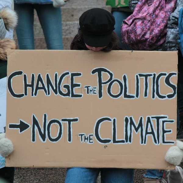 Demonstrator holding a sign reading "CHANGE THE POLITICS, NOT THE CLIMATE"