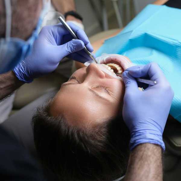 Dental tech with blue gloves with hands and instruments in patient's mouth