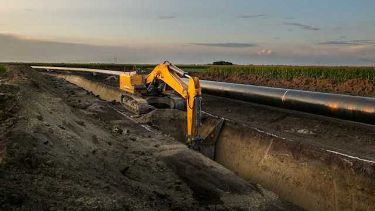 Digging equipment deepening a trench with a pipeline sitting above it