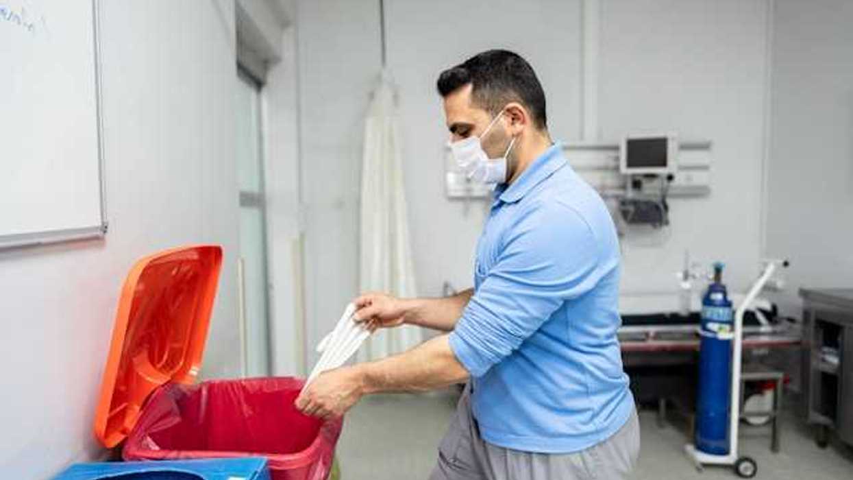 Doctor disposing of plastic glove in a red medical bin