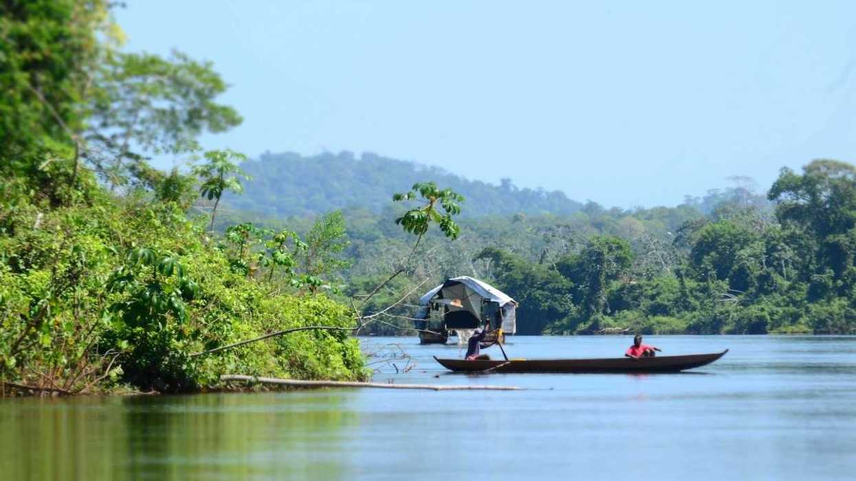 Dugout canoe with two passengers on a river in a rainforest/jungle setting.