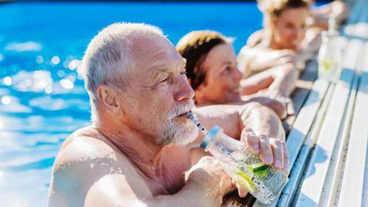 Elderly white man in a pool drinking from a straw