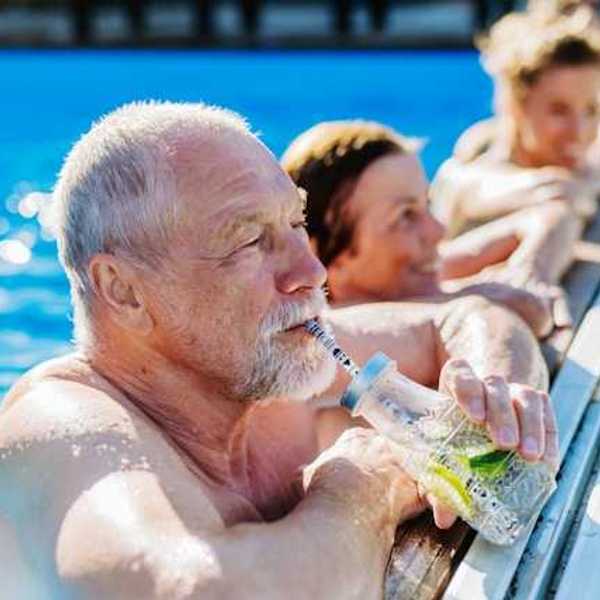Elderly white man in a pool drinking from a straw