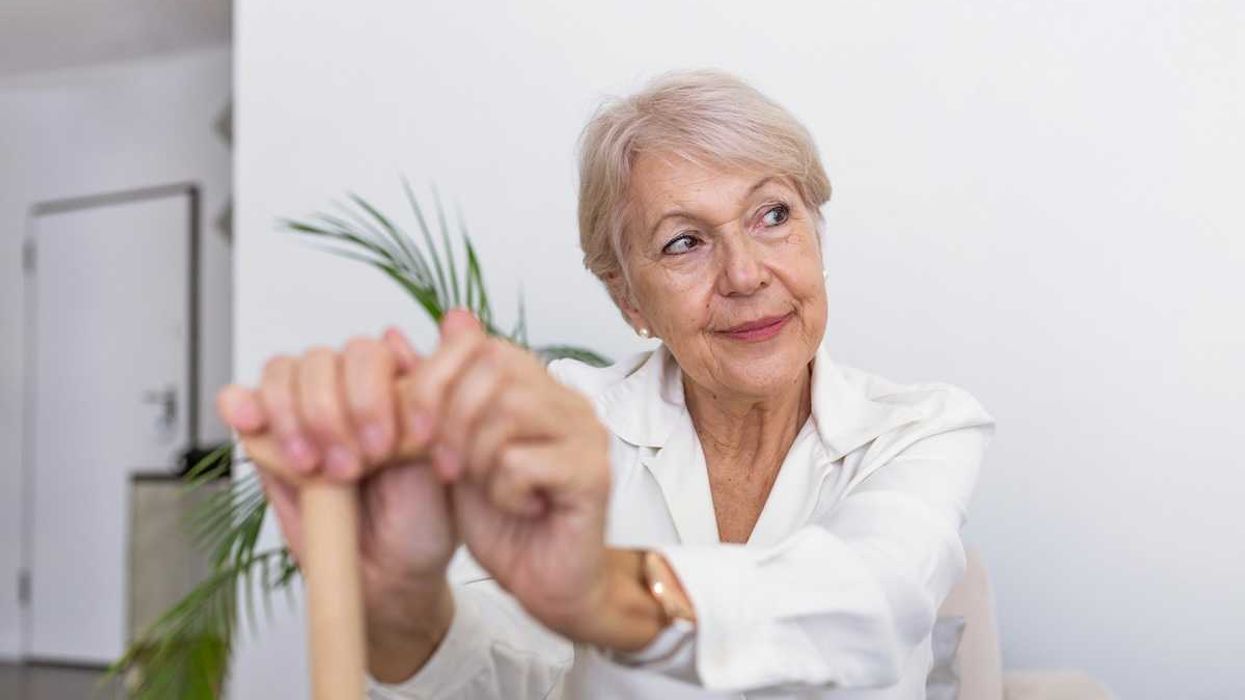 Elderly woman seated with hands resting on cane