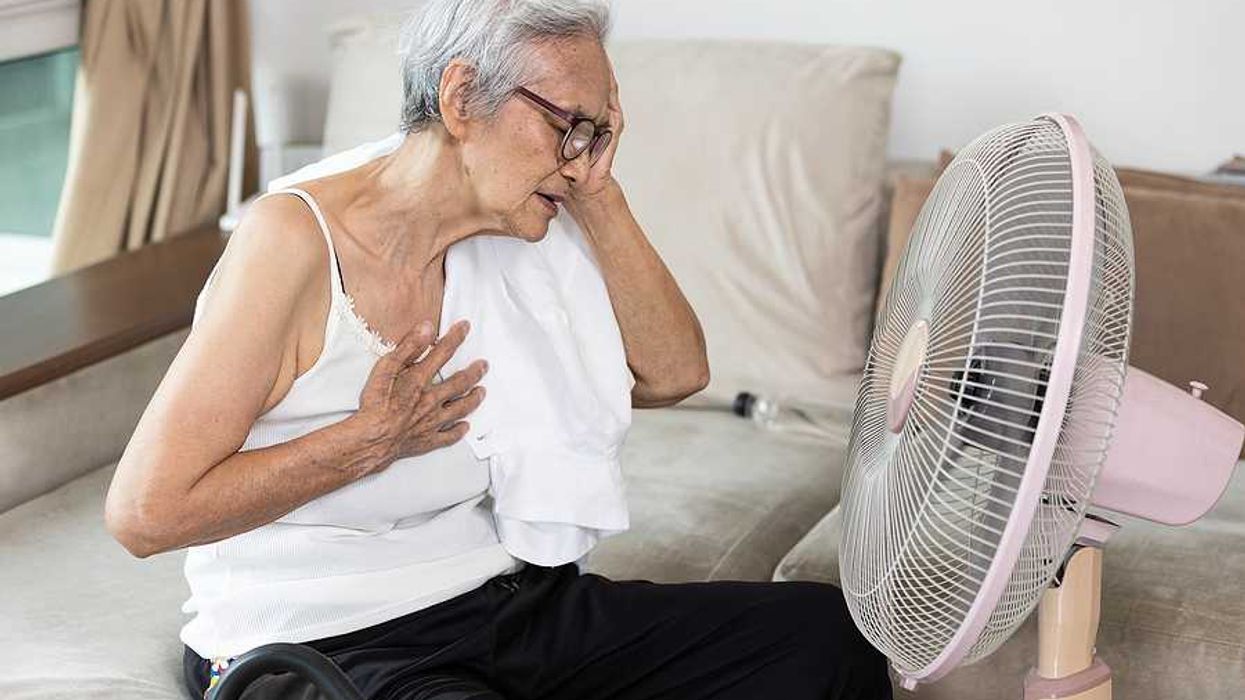 Elderly woman sitting in front of a fan with her hand to her head