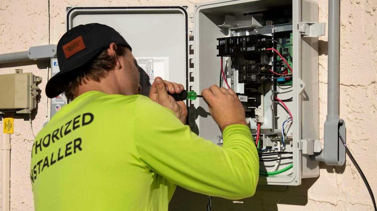 Electrician in yellow-green shirt using a screwdriver while working on an electrical service panel