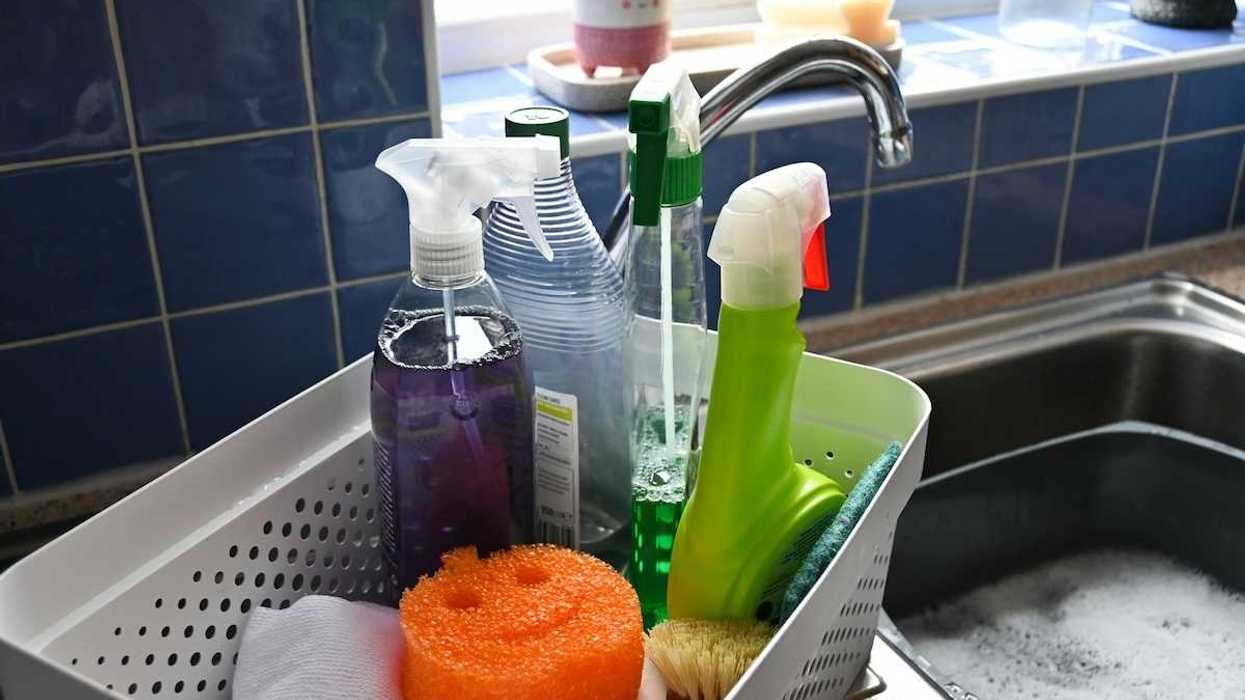 Everyday household cleaning supplies adjacent to a sink with a plastic dishpan containing sudsy dishwater