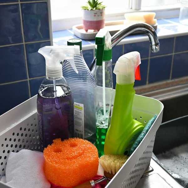 Everyday household cleaning supplies adjacent to a sink with a plastic dishpan containing sudsy dishwater