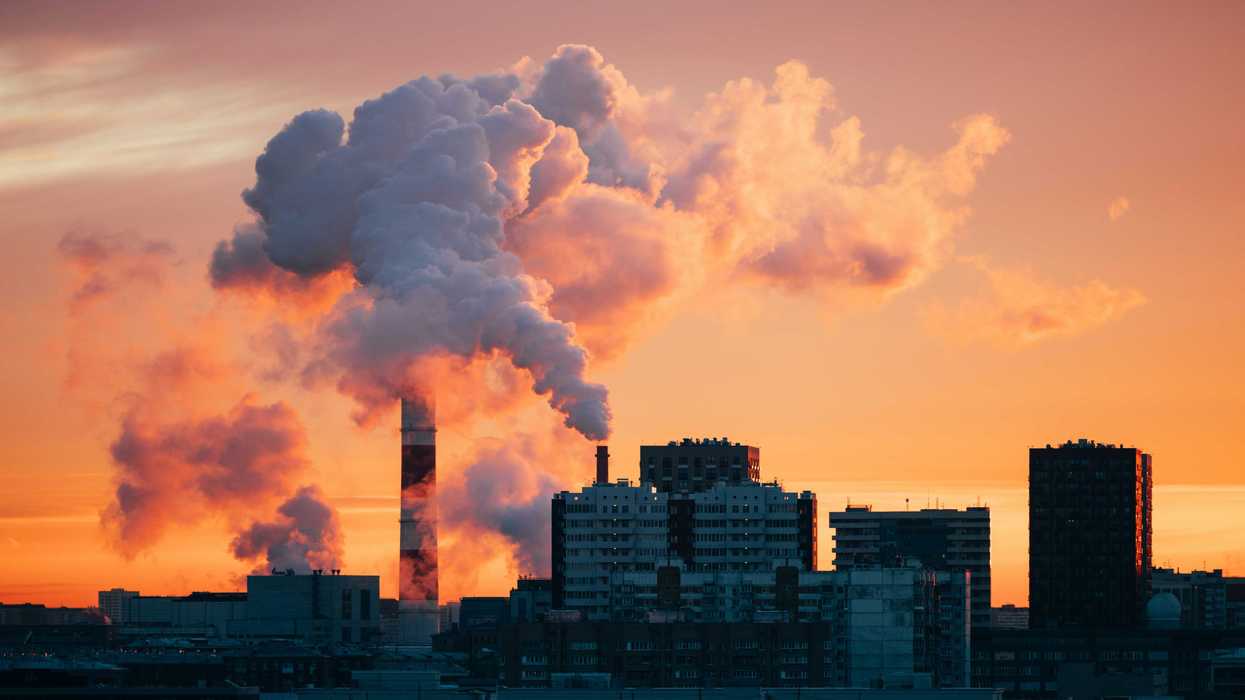 Factory smokestacks emitting smoke against sunset sky.