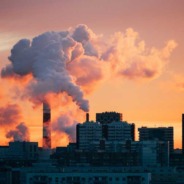Factory smokestacks emitting smoke against sunset sky.