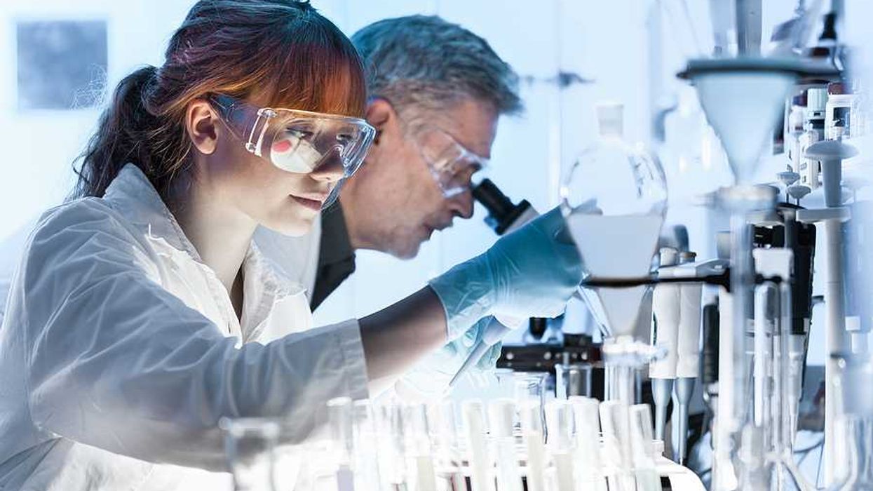 Female research scientist and male scientist preparing and analyzing microscope slides in research lab.
