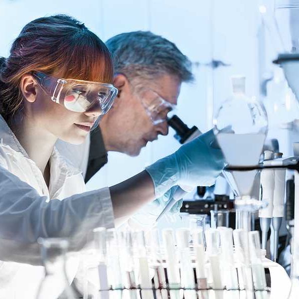 Female research scientist and male scientist preparing and analyzing microscope slides in research lab.