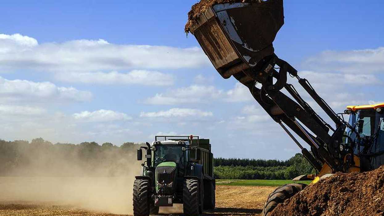 Field excavator with a shovel full of biosolids ready to fill the trailer of the tractor, prior to spreading on fields.