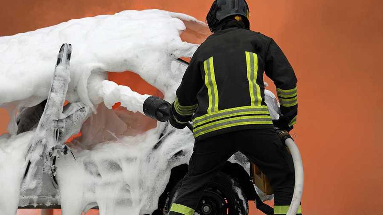 Firefighter demonstrating extinguishing a car fire with aqueous firefighting foam.