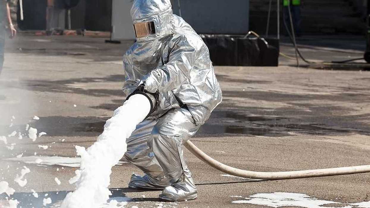Firefighter dressed in protective suit spraying fire with firefighting foam
