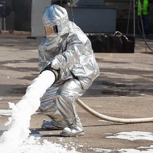 Firefighter dressed in protective suit spraying fire with firefighting foam