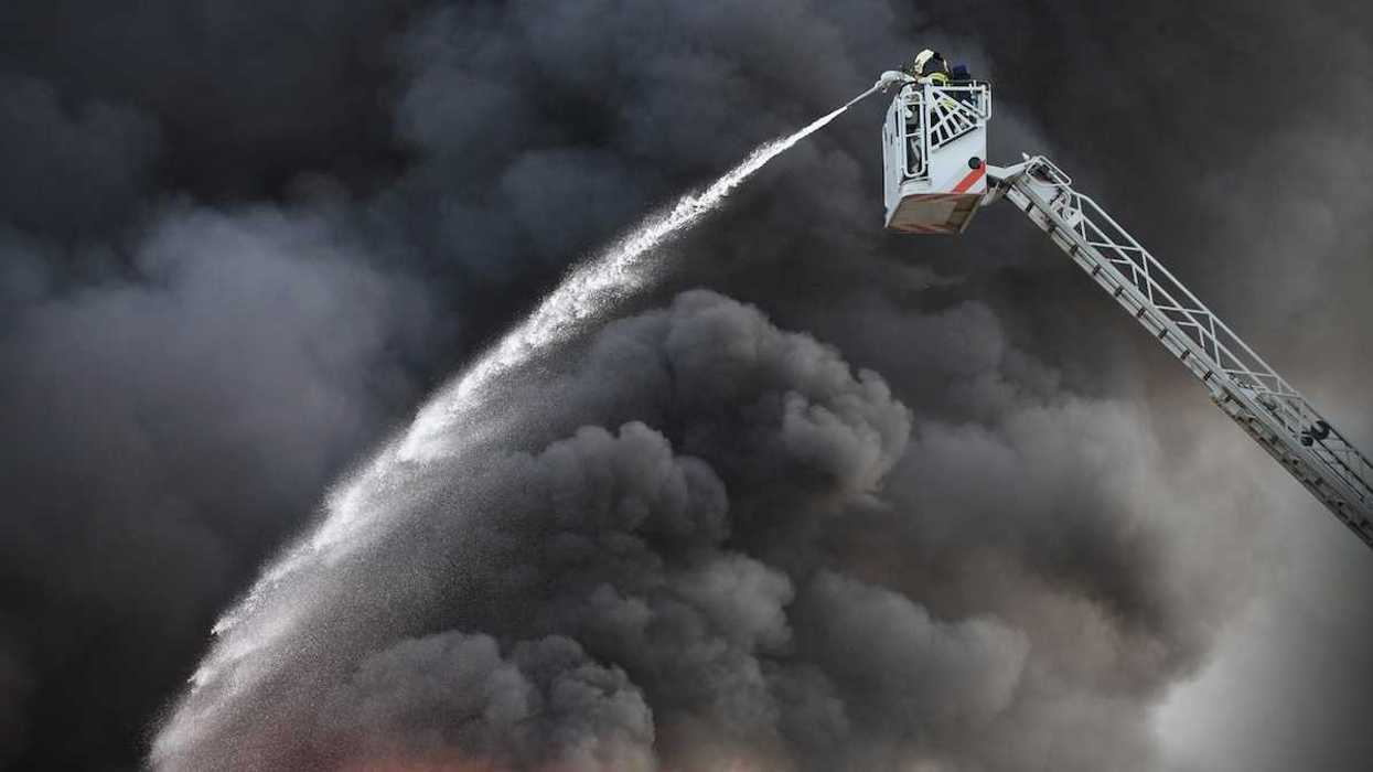 Firefighter hosing down a factory fire from an aerial bucket