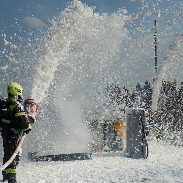 Firefighter in turnout gear covering the surrounding area in toxic firefighting foam during training exercise.