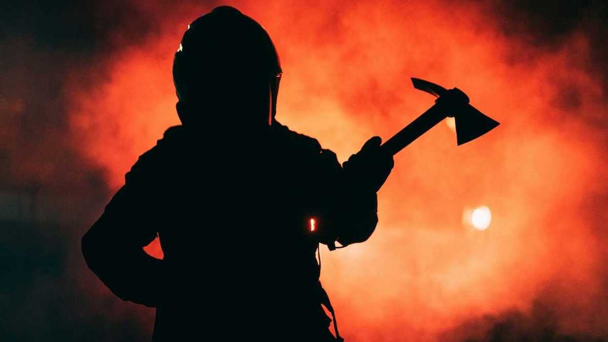 Firefighter wielding a Pulaski tool silhouetted against inferno