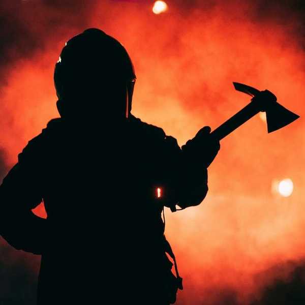 Firefighter wielding a Pulaski tool silhouetted against inferno