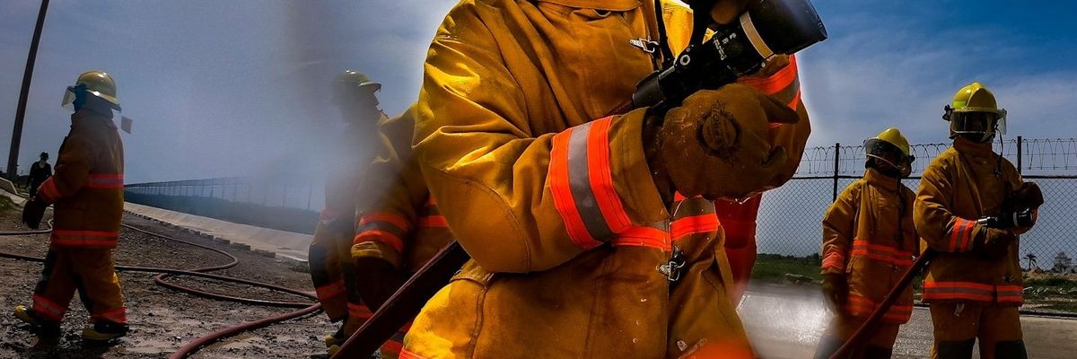 Firefighters in orange protective gear holding a water hose.