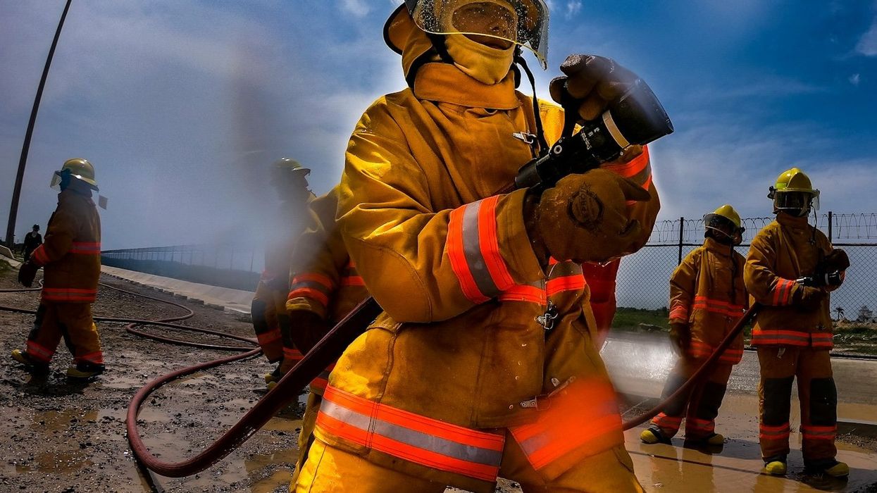 Firefighters in orange protective gear holding a water hose.