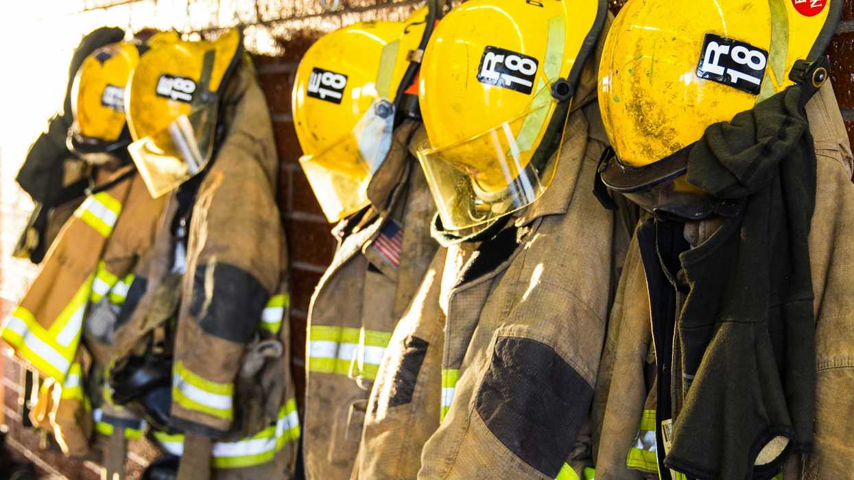 Firefighting uniforms and helmets hanging in a row.