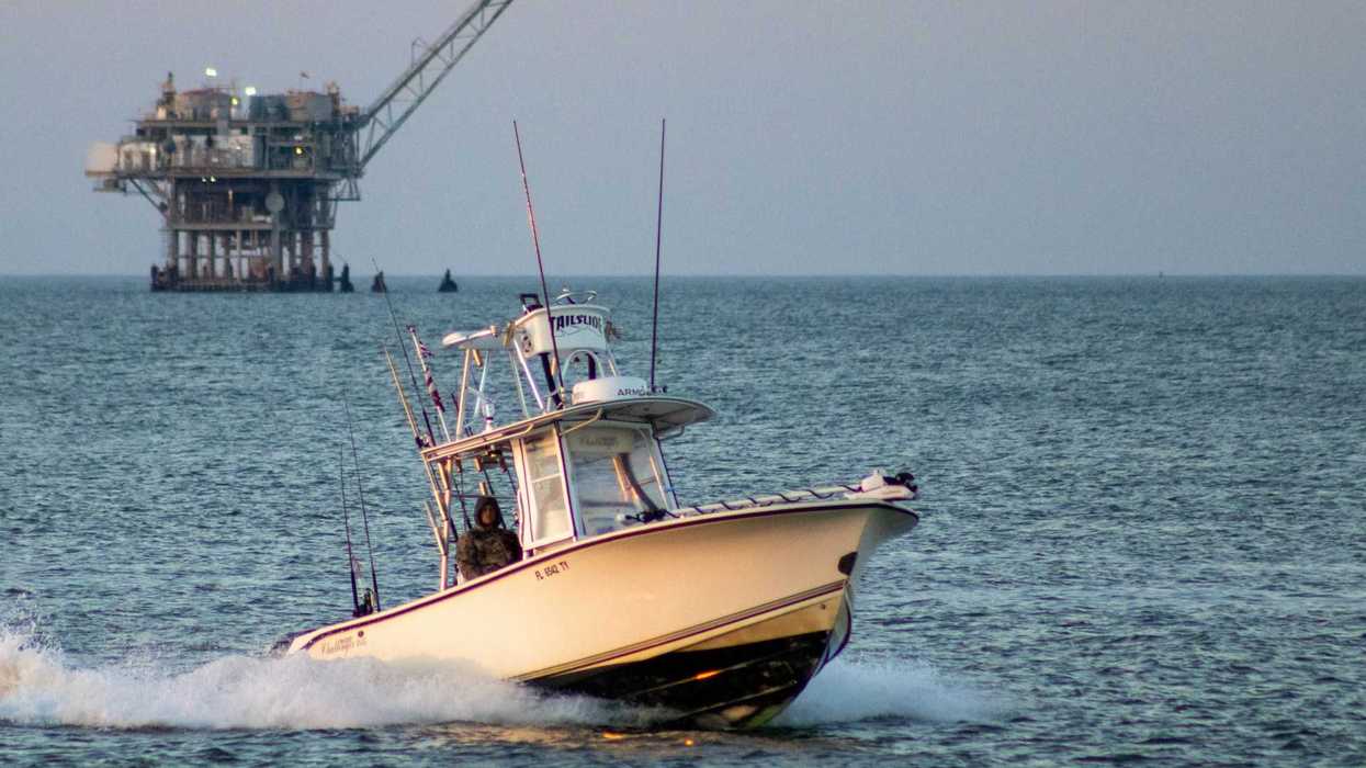 Fishing boat on open water with oil drilling rig in the background