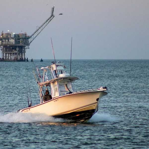 Fishing boat on open water with oil drilling rig in the background