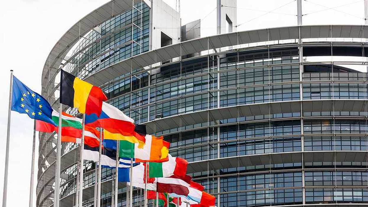 Flags of the EU flying outside a glass and steel building