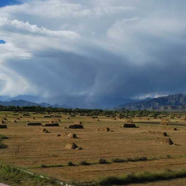 Flat valley in mountainous western state with haystacks and storm moving through valley
