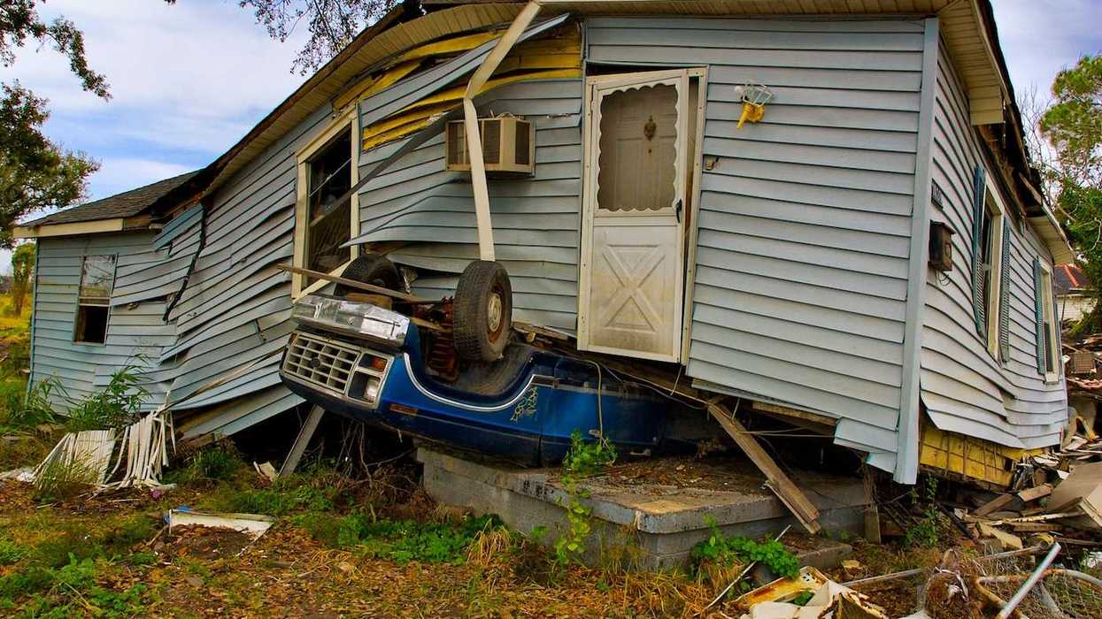 Flood aftermath with House sitting on an overturned blue Ford pickup truck.