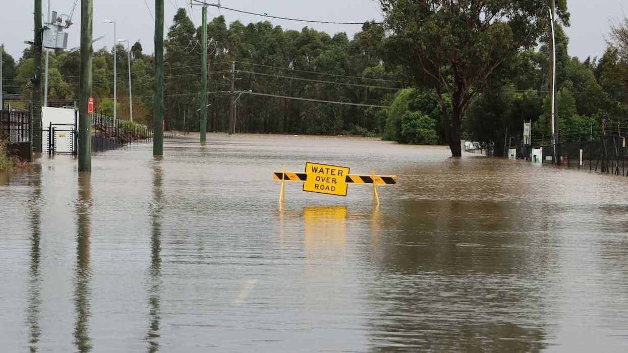 Flooded street with a yellow sign reading "water over road"