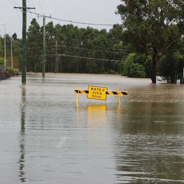 Flooded street with a yellow sign reading "water over road"