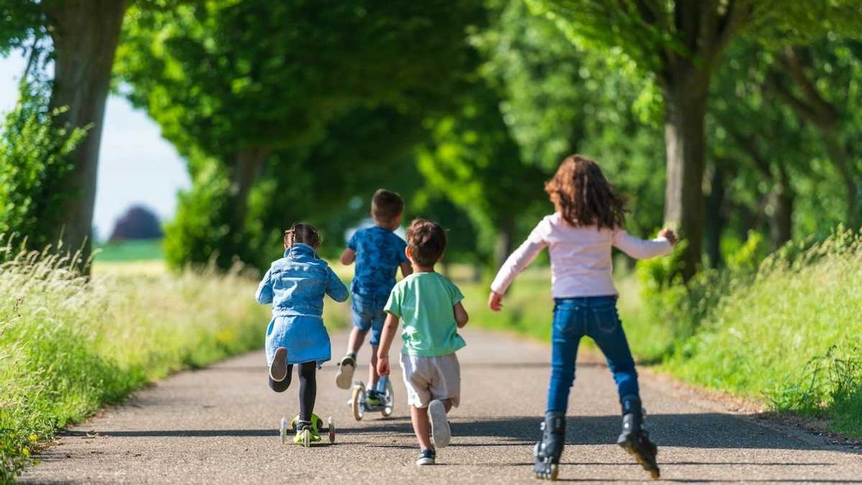 Four children playing - running, roller blading, pushing scooters along a surfaced trail