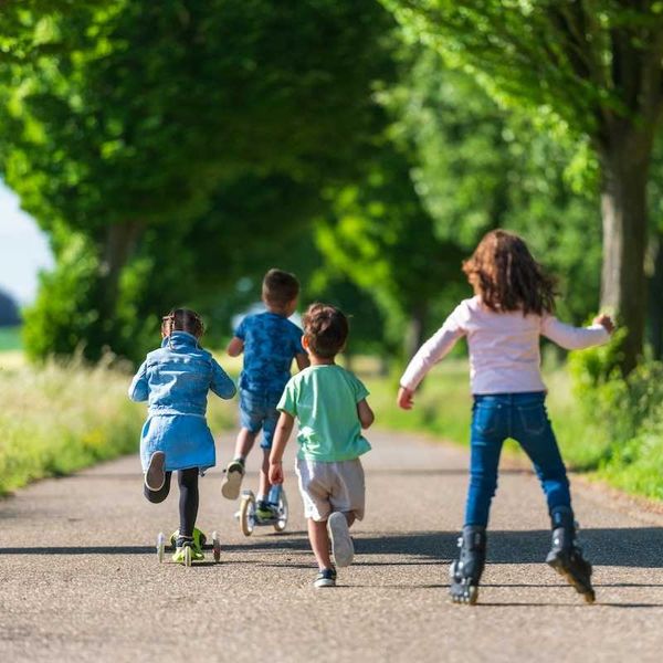 Four children playing - running, roller blading, pushing scooters along a surfaced trail