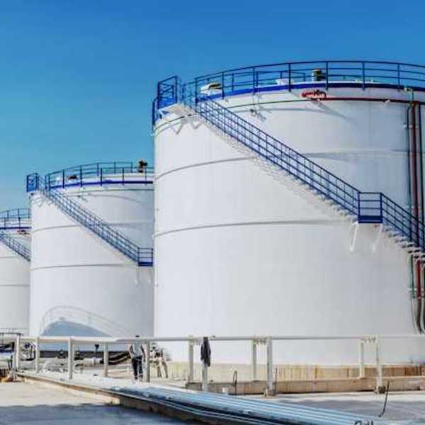 Four circular white industrial tanks with blue staircases against a blue sky