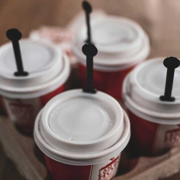 four white disposable lidded cups in a cardboard to-go holder.