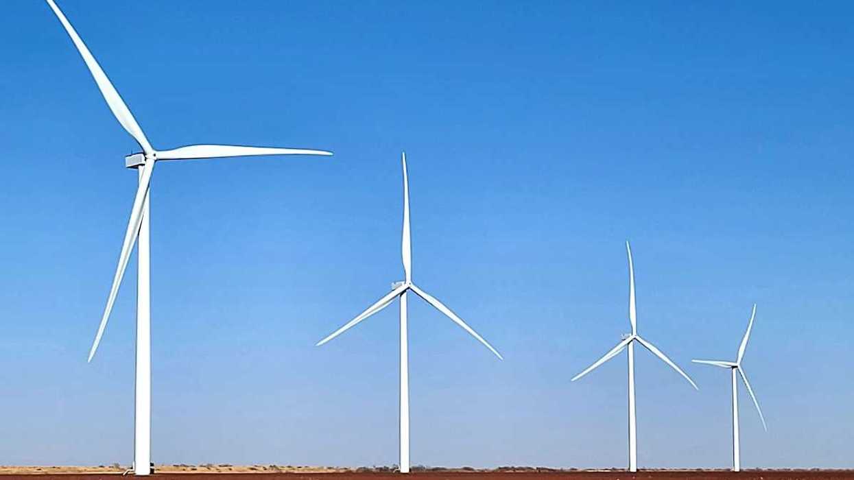 Four wind turbines in a row standing in a flat brown field.