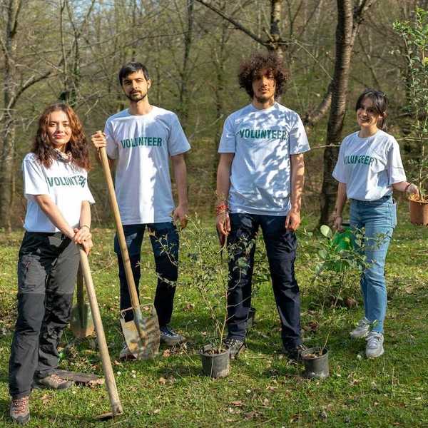 Four young people wearing t-shirts that read "volunteers" equipped to plant trees.