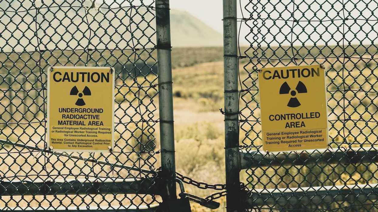 Galvanized pipe and mesh fencing with padlocked chain discouraging entry to underground nuclear waste disposal site.