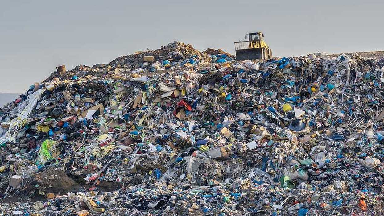 Garbage pile in trash dump or landfill with yellow bucket loader perched at the top of the pile.