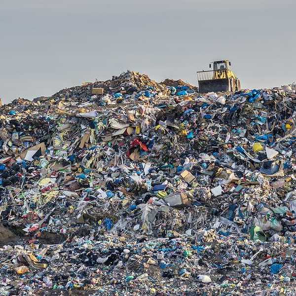 Garbage pile in trash dump or landfill with yellow bucket loader perched at the top of the pile.