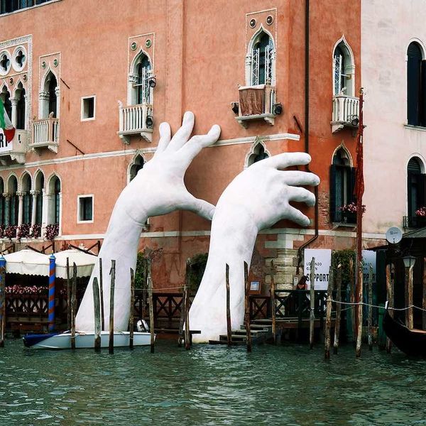 Gigantic hands rise from water to support the Ca' Sagredo Hotel, a statement of the impact of climate change and rising sea levels.