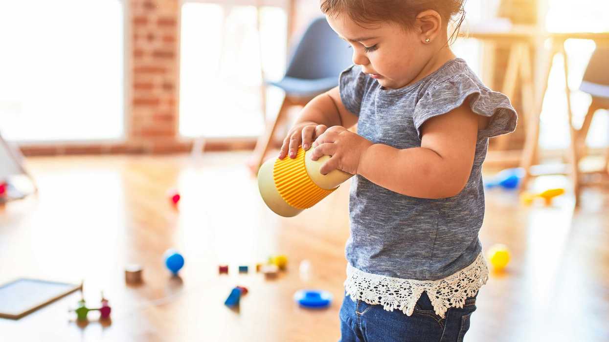 girl in blue denim dungaree pants holding yellow object with plastic toys in background.