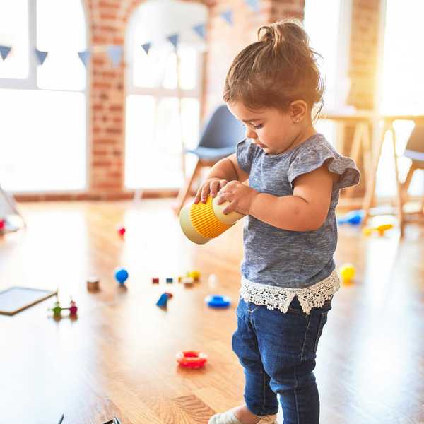 girl in blue denim dungaree pants holding yellow object with plastic toys in background.