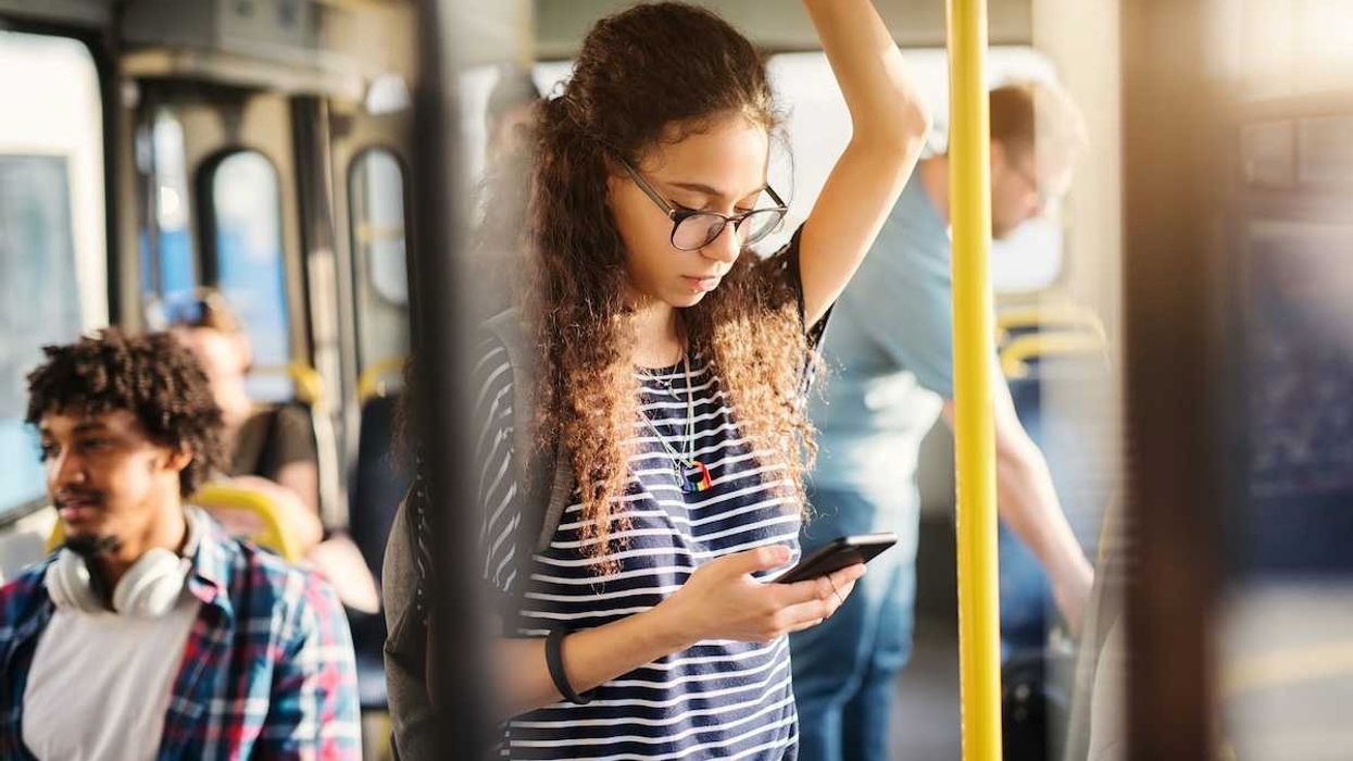Girl riding bus while standing and checking cell phone
