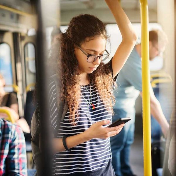 Girl riding bus while standing and checking cell phone