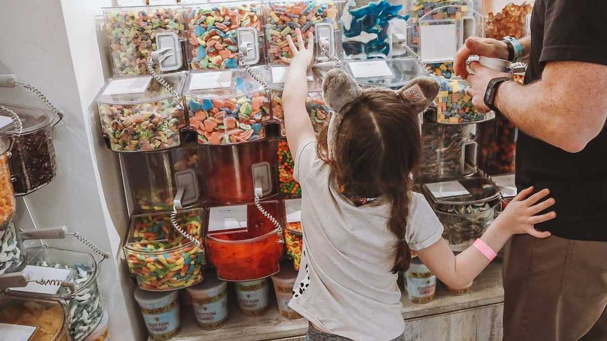 Girl standing with an adult, choosing candy at "bulk candy" counter in candy store.