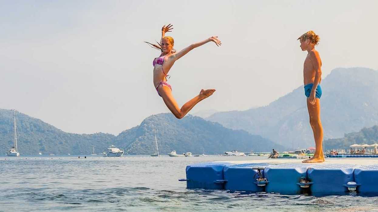 Girl striking a mid-air pose while jumping into water - boy stands and waits his turn